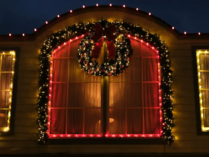 Arched window framed in lights and garland with a lit wreath